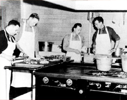 Two men prepare food for cooking while an instructor works with another.
